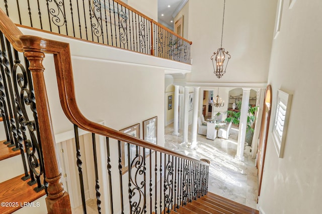 staircase with a notable chandelier, a towering ceiling, and ornate columns