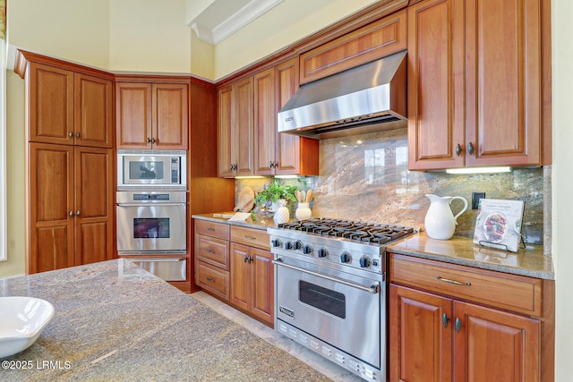 kitchen with brown cabinets, light stone counters, stainless steel appliances, and exhaust hood