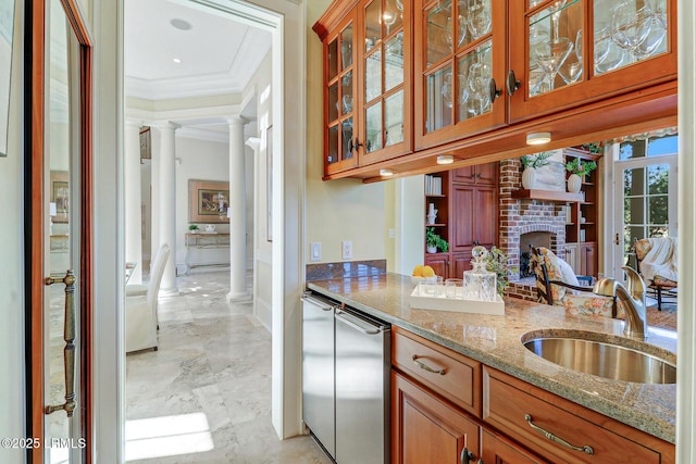 kitchen with light stone counters, brown cabinets, crown molding, a sink, and ornate columns