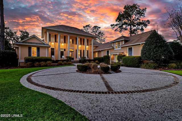 neoclassical / greek revival house featuring curved driveway, a lawn, and stucco siding