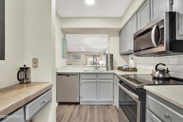 kitchen with tasteful backsplash, appliances with stainless steel finishes, gray cabinetry, and light hardwood / wood-style flooring