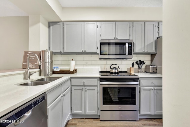 kitchen with sink, gray cabinets, stainless steel appliances, light hardwood / wood-style floors, and backsplash