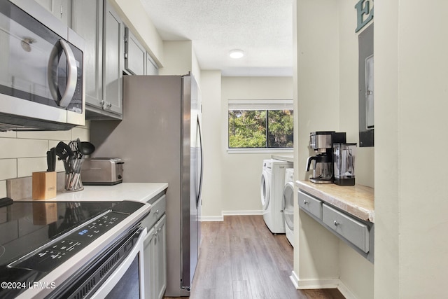 kitchen with appliances with stainless steel finishes, a textured ceiling, washer and dryer, and gray cabinetry