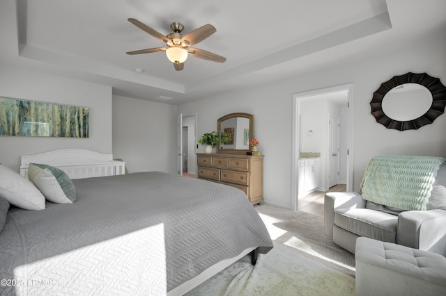 bedroom featuring baseboards, ceiling fan, light carpet, a raised ceiling, and connected bathroom