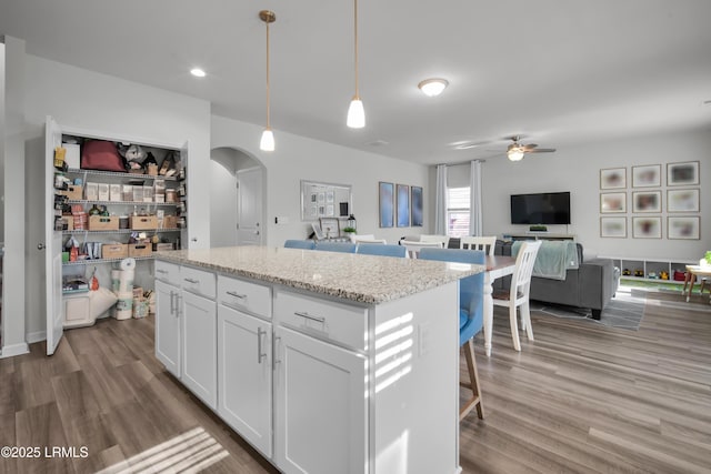 kitchen with wood finished floors, arched walkways, open floor plan, and ceiling fan