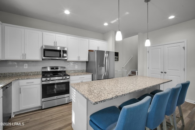 kitchen with a breakfast bar, decorative backsplash, appliances with stainless steel finishes, wood finished floors, and white cabinets