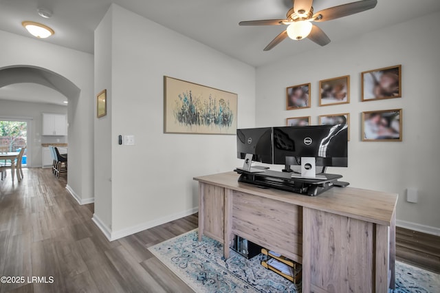 home office with arched walkways, baseboards, ceiling fan, and wood finished floors