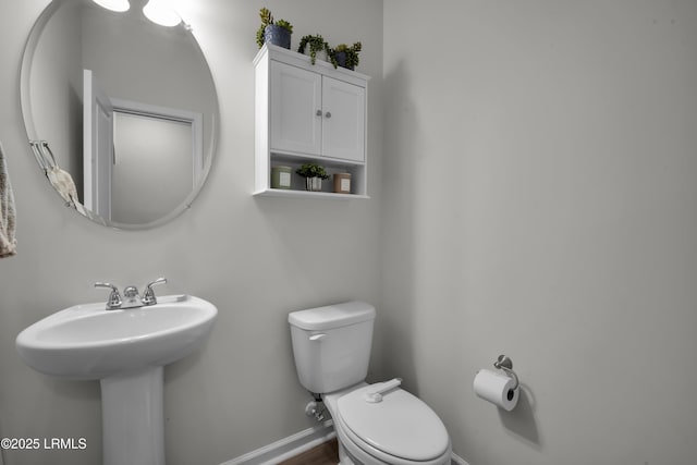 half bath featuring baseboards and toilet