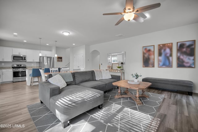 living room with arched walkways, recessed lighting, light wood-type flooring, and a ceiling fan