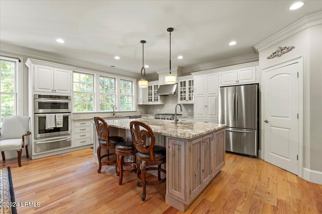 kitchen with white cabinetry, stainless steel appliances, light stone counters, and a center island with sink