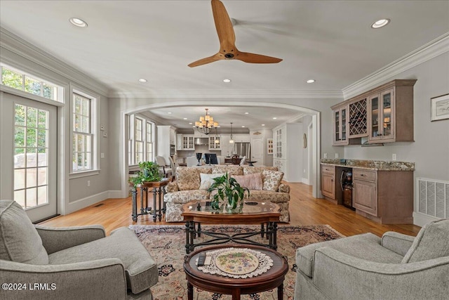 living room with indoor bar, light wood-type flooring, wine cooler, ornamental molding, and an inviting chandelier