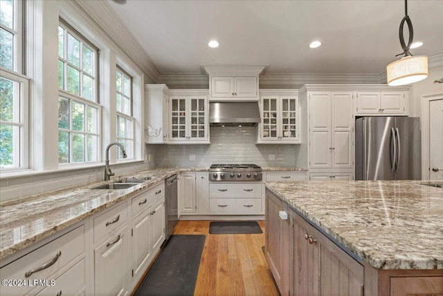 kitchen featuring pendant lighting, sink, stainless steel appliances, white cabinets, and wall chimney exhaust hood