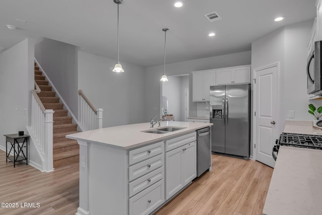 kitchen featuring a center island with sink, appliances with stainless steel finishes, light countertops, white cabinetry, and pendant lighting