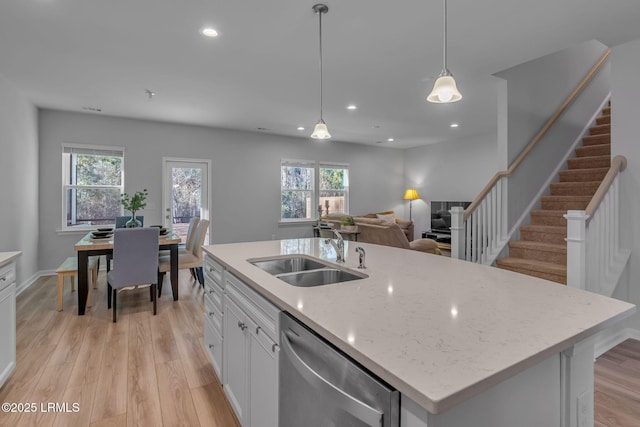 kitchen featuring decorative light fixtures, stainless steel dishwasher, a kitchen island with sink, a sink, and white cabinetry