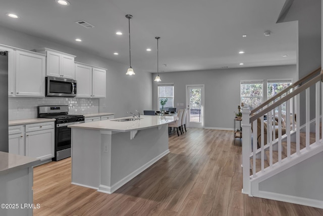 kitchen featuring a kitchen island with sink, a sink, white cabinets, appliances with stainless steel finishes, and pendant lighting