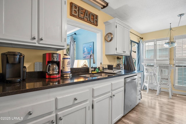 kitchen featuring white cabinetry, a sink, light wood-type flooring, dishwasher, and hanging light fixtures