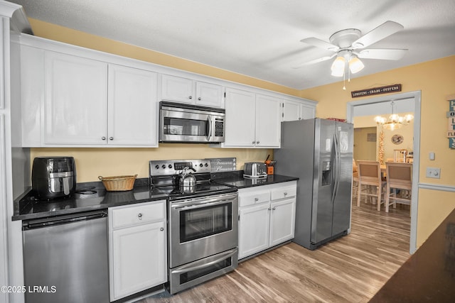 kitchen featuring light wood-style floors, appliances with stainless steel finishes, white cabinets, ceiling fan with notable chandelier, and dark countertops