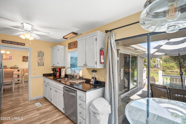 kitchen with a sink, light wood-style flooring, white cabinetry, stainless steel dishwasher, and dark countertops