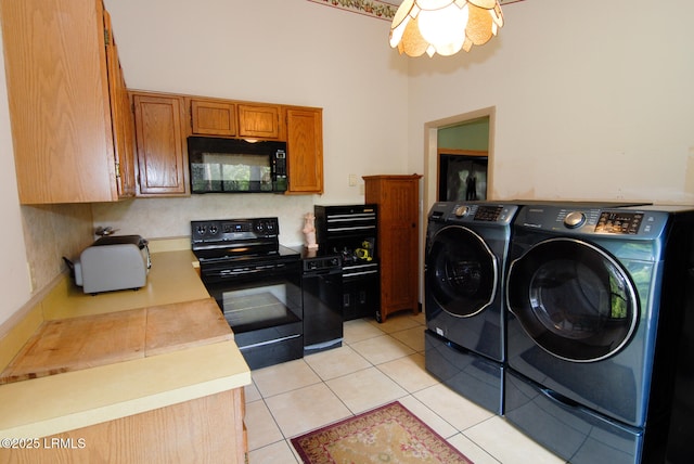 kitchen with brown cabinetry, light tile patterned flooring, washer and clothes dryer, light countertops, and black appliances