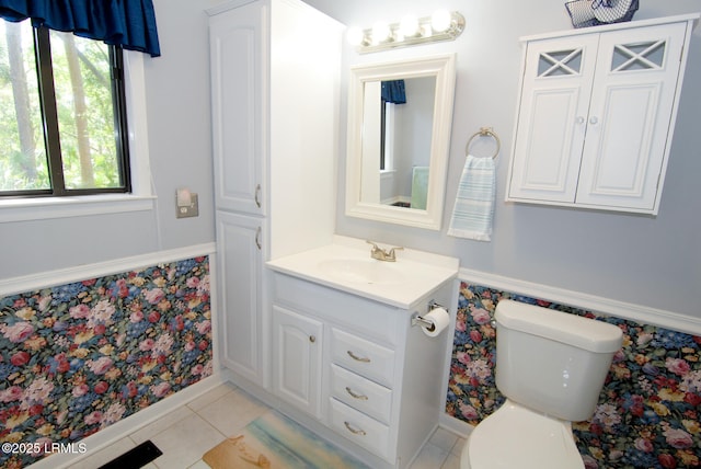 bathroom with tile patterned flooring, wainscoting, vanity, toilet, and wallpapered walls