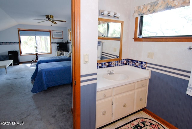 ensuite bathroom featuring ceiling fan, a healthy amount of sunlight, lofted ceiling, and vanity