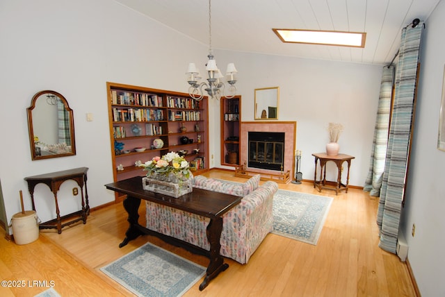 living area with vaulted ceiling with skylight, a tiled fireplace, wood finished floors, baseboards, and a chandelier