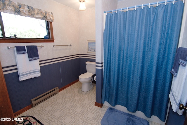 full bath with a shower with shower curtain, toilet, baseboard heating, and a wainscoted wall