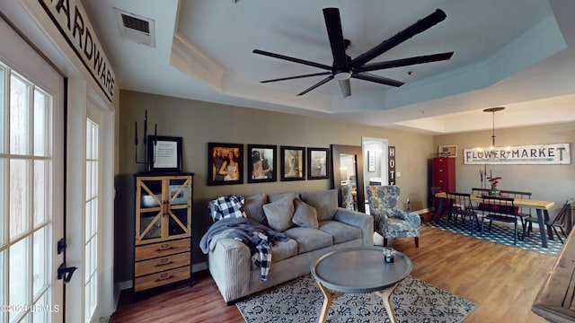 living room with a raised ceiling, ceiling fan with notable chandelier, and hardwood / wood-style floors