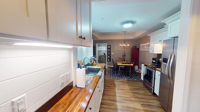 kitchen featuring decorative light fixtures, butcher block counters, sink, a tray ceiling, and stainless steel appliances