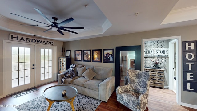 living room featuring a raised ceiling, ornamental molding, hardwood / wood-style flooring, and french doors