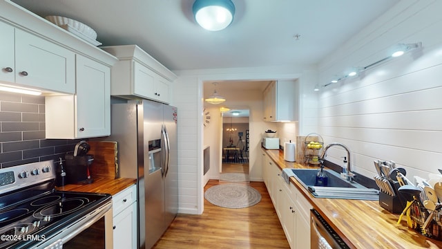 kitchen with butcher block countertops, sink, stainless steel appliances, white cabinets, and decorative backsplash