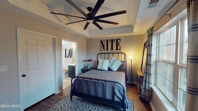 bedroom featuring dark hardwood / wood-style floors, ceiling fan, connected bathroom, and a tray ceiling