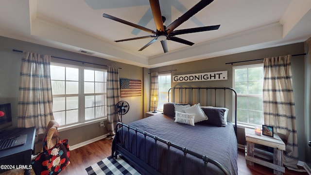 bedroom featuring dark wood-type flooring, ornamental molding, a raised ceiling, and ceiling fan