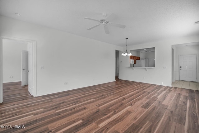 unfurnished living room with dark hardwood / wood-style floors, ceiling fan with notable chandelier, and a textured ceiling