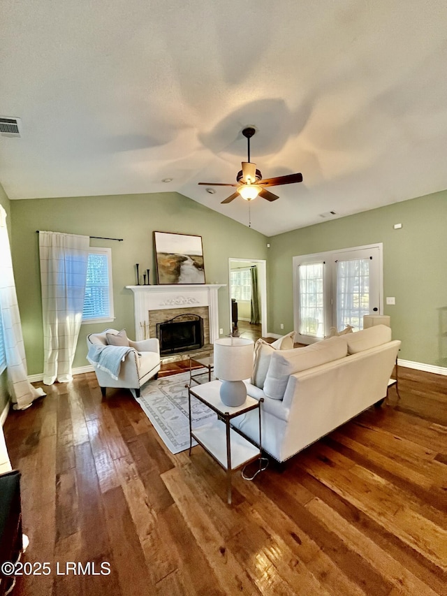 living room featuring a fireplace with raised hearth, a wealth of natural light, lofted ceiling, and dark wood finished floors