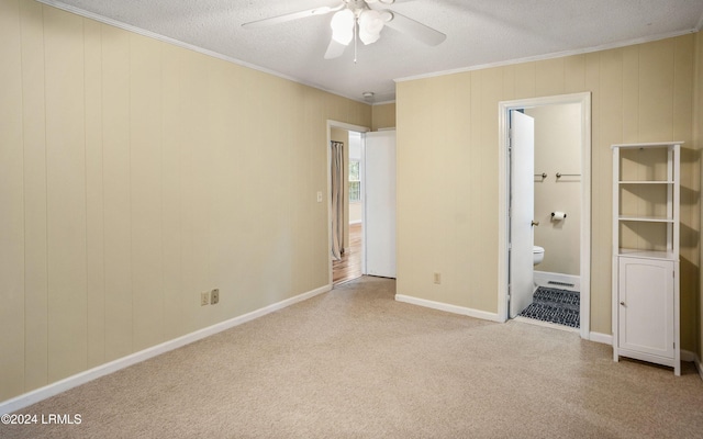 unfurnished bedroom featuring ensuite bath, ornamental molding, light colored carpet, ceiling fan, and a textured ceiling