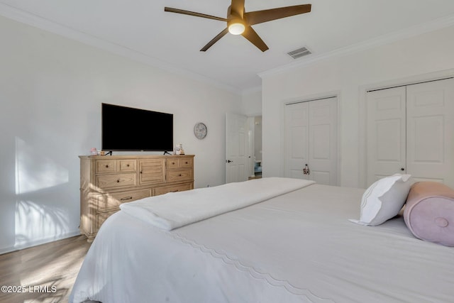 bedroom with multiple closets, crown molding, wood-type flooring, and ceiling fan