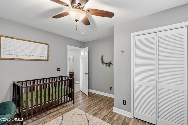 bedroom with a closet, ceiling fan, wood finished floors, a crib, and baseboards