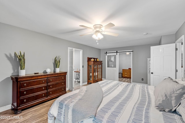 bedroom with a barn door, baseboards, light wood-style flooring, and a ceiling fan