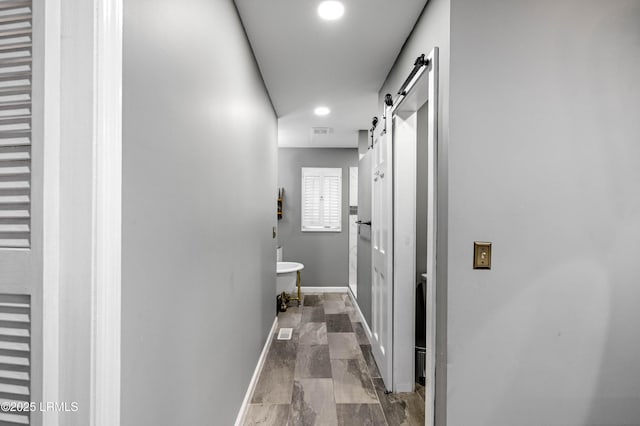 corridor featuring a barn door, baseboards, and recessed lighting