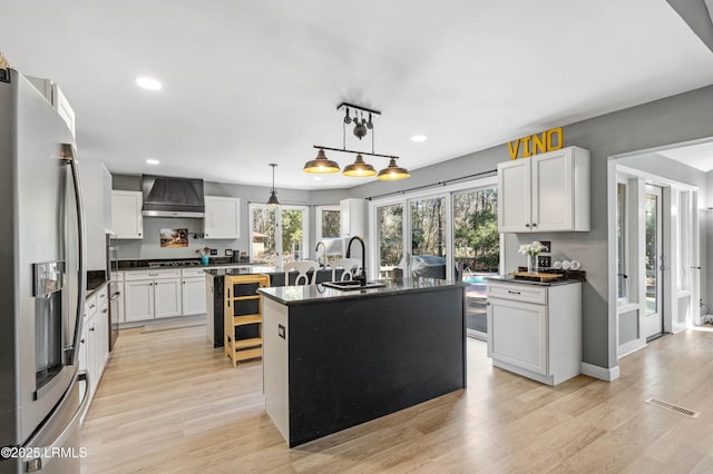 kitchen with a sink, visible vents, stainless steel fridge with ice dispenser, a center island with sink, and custom range hood