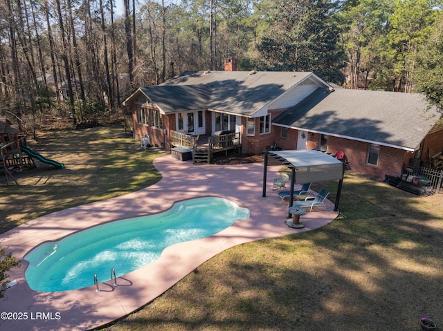 outdoor pool with a patio area, a playground, a wooden deck, and a lawn