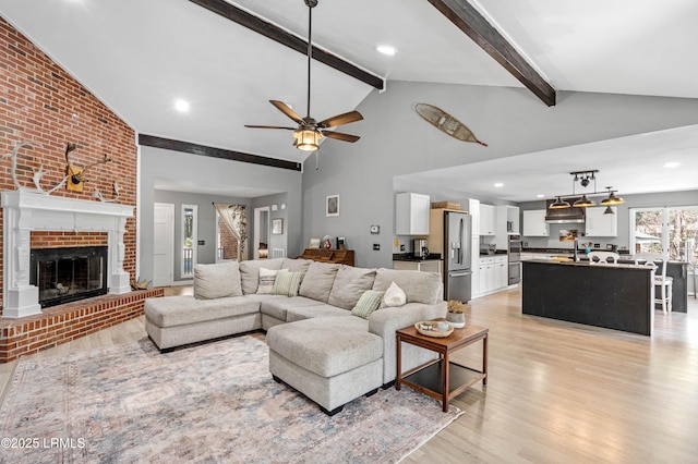 living room featuring beam ceiling, a fireplace, a ceiling fan, light wood-style floors, and high vaulted ceiling