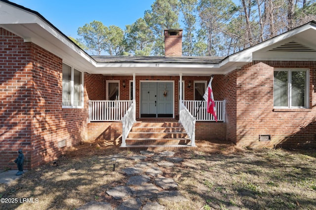 doorway to property with a porch, crawl space, brick siding, and a chimney