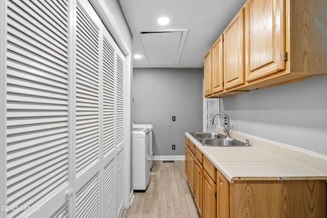 clothes washing area featuring laundry area, attic access, light wood finished floors, washer and clothes dryer, and a sink