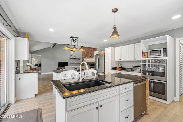 kitchen with appliances with stainless steel finishes, open floor plan, white cabinets, a sink, and an island with sink