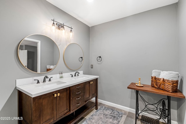 bathroom with double vanity, wood finished floors, a sink, and baseboards