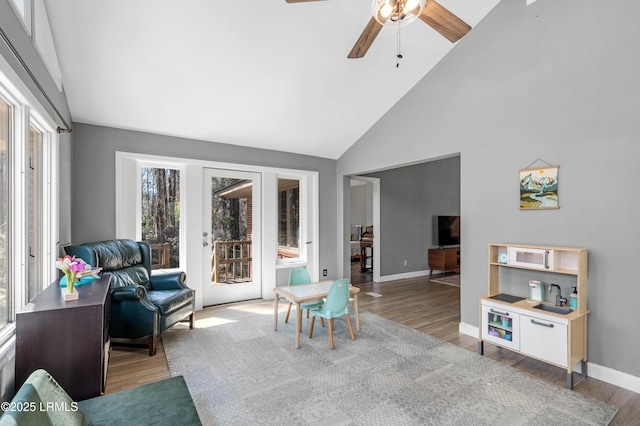 living area featuring ceiling fan, high vaulted ceiling, wood finished floors, and baseboards