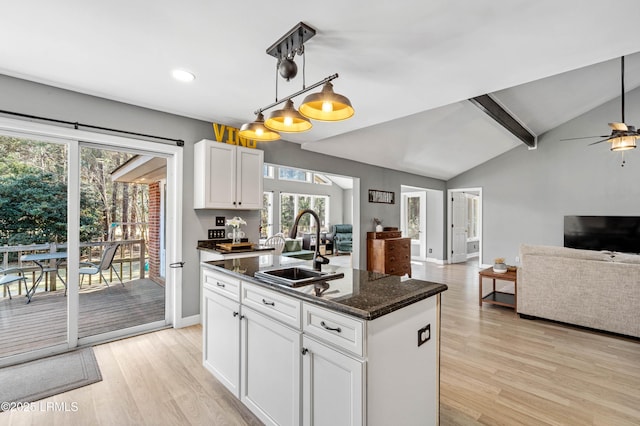 kitchen with vaulted ceiling with beams, light wood-style flooring, a sink, white cabinets, and open floor plan