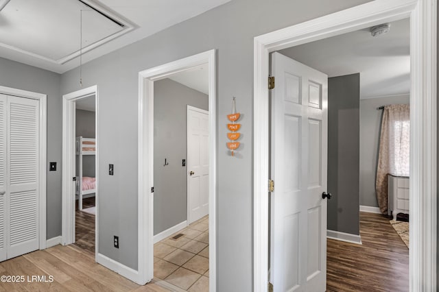 hall with light wood-style floors, attic access, visible vents, and baseboards